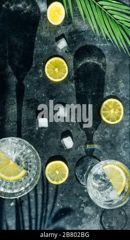 Acqua limone detox. Acqua fredda pura con limone in bicchieri di cristallo su sfondo scuro al sole estivo. Foto Stock