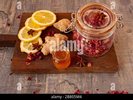 Un vaso di petali di rosa secchi, miele e zenzero, e condimenti aromatici su un asse di legno. Foto Stock