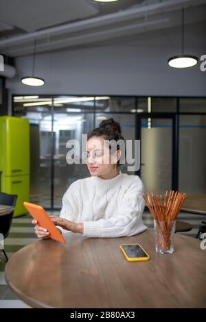 Giovane donna seduta al tavolo, con occhiali, tavoletta a scorrimento Foto Stock