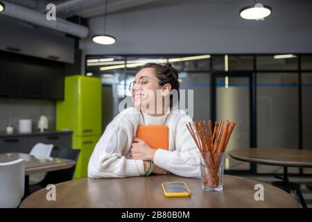 Giovane donna seduta al tavolo, tenendosi stretto il suo tablet Foto Stock
