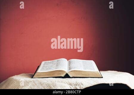 Aprire la Sacra Bibbia su un tavolo. Bellissimo sfondo rosso parete. Foto Stock