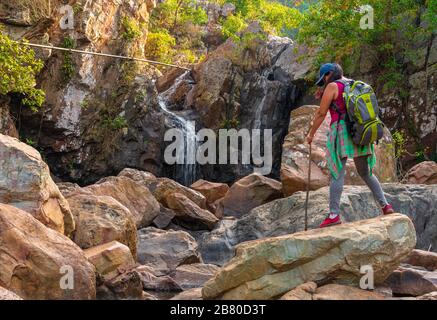 Un viaggiatore indiano solista Lady godere della vista di una cascata che trasporta il suo zaino. Foto Stock