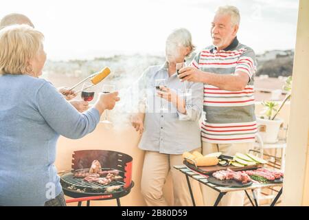 Amici anziani felici che si divertono al barbecue pasto nel patio all'aperto - anziani maturi cena e bere vino al barbecue pranzo - Focus sulla mano sinistra della donna Foto Stock