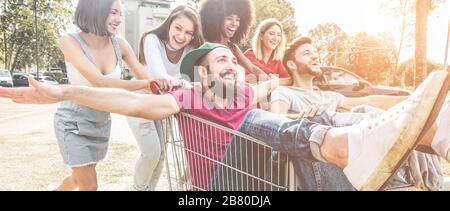 Giovani millennials persone che corrono con il carrello - amici folli felici divertirsi con i carrelli nel parcheggio - stile di vita giovanile e concetto di festa - Fo Foto Stock