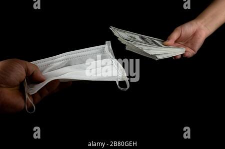 Primo piano Vendita acquistare maschera viso medico, mano tenendo maschera medico protezione antivirus e denaro di 100 dollari di banconote un sacco di sfondo nero, esso Foto Stock