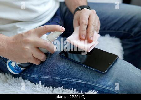 un uomo spruzza sullo smartphone un igienizzante per disinfettare e prevenire le malattie virali. Agente antimicrobico antibatterico per l'uccisione di microbi. Età di pulizia Foto Stock