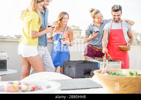 Felice studenti che cucinano e bevono vino al barbecue party pranzo - migliori amici grigliare carne con salsa barbecue - stile di vita giovanile, cibo, amicizia conce Foto Stock