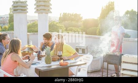 Amici felici mangiare e bere vino rosso al barbecue party - giovani grigliate e divertirsi al barbecue cena all'aperto - Focus sui ragazzi di destra sittin Foto Stock