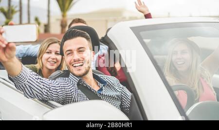 Amici felici che fanno un selfie video streaming in auto convertibile in vacanza estiva - giovani che si divertono con la tecnologia di tendenze - Focus su MAN wi Foto Stock