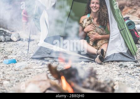 Gli escursionisti accampano in montagna di roccia con il loro cane - gente sportiva che si rilassa dopo una giornata di arrampicata facendo fuoco accanto alla tenda - Viaggi, natura li Foto Stock