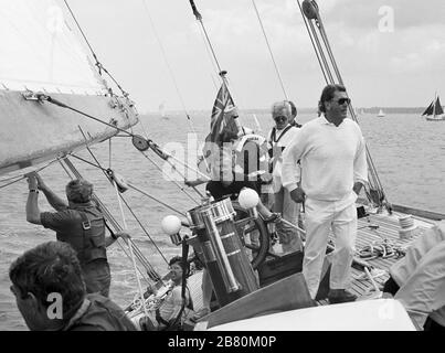 Helmsman concentrando, circondato da afterguard a bordo dello yacht di classe J 'Velsheda' (K7): vela nel Solent dopo la prima reinstallazione, estate 1991. Archivia la fotografia di film in bianco e nero Foto Stock