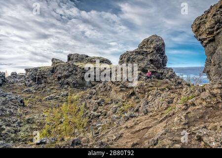 Donna che ammirava Dimmuborgir, un labirinto di enormi monoliti lavici, torri e caverna vicino al lago Myvatn nel nord dell'Islanda Foto Stock