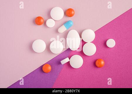 Pillole e compresse su sfondo rosa, viola e viola, concetto medico sanitario, antibiotici e cure, vista dall'alto Foto Stock