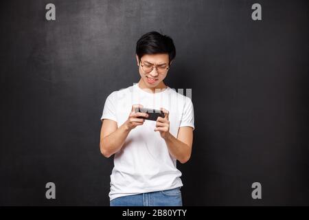 Tecnologia, gadget e concetto di persone. Ritratto di concentrato, ragazzo asiatico concentrato cercando uccidere mob nel gioco mobile, passando arcade o gare di strada Foto Stock