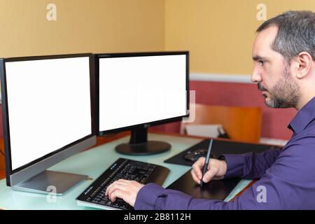 uomo che lavora in casa con due schermi Foto Stock