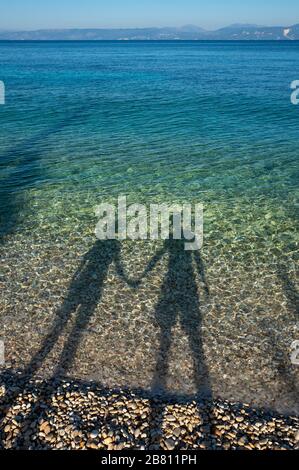 una coppia amorevole su una spiaggia che crea ombre nel mare Foto Stock