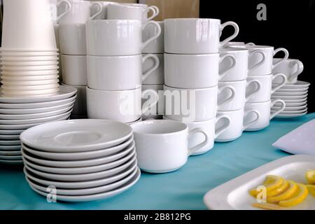 Esposti su pile di tazze bianche e piattini in ceramica pulita. I piatti del ristorante sono preparati per bere il tè e il caffè. Foto Stock