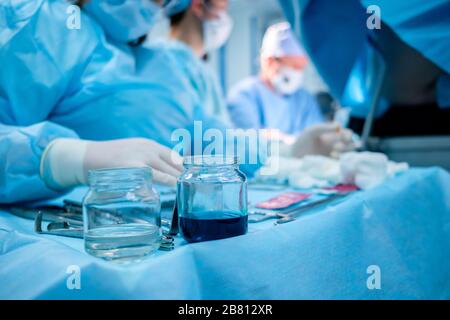 Strumenti chirurgici sterili e contenitori in vetro con soluzioni speciali sul tavolo durante un intervento chirurgico. Su uno sfondo molto sfocato, surgeo Foto Stock