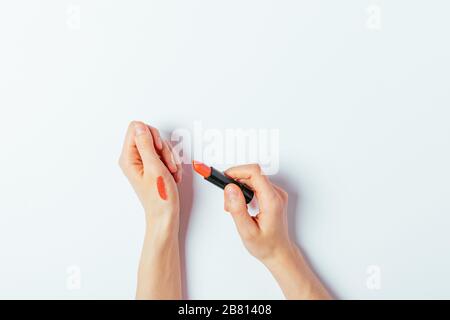 Le mani della donna applicano la linea del rossetto rosso sulla pelle per determinare il colore, vista dall'alto. Foto Stock