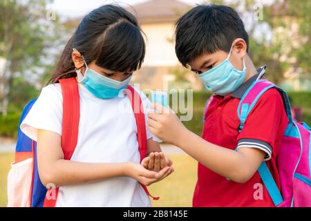 I ragazzi asiatici indossano una maschera igienica e premono il gel d'alcol dalla bottiglia alla sorella della mano per proteggere il coronavirus covid-19 e il virus epidemico dopo bac Foto Stock