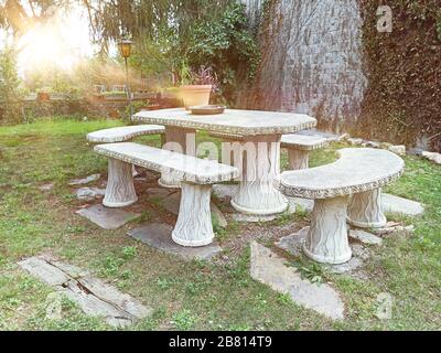 Patio con panca in pietra in un'area salotto di un giardino con erba verde e piante. Ora del tramonto e spazio di copia vuoto per il contenuto dell'Editor. Foto Stock