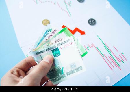 Uomo mano che tiene ruble fatture sul tasso di cambio di rublo russo e freccia rossa. Deprezzamento rublo. Tasso di cambio di caduta rublo. Rouble a dollaro Foto Stock