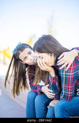 Giovane donna conforta una triste amica femminile nel parco Foto Stock