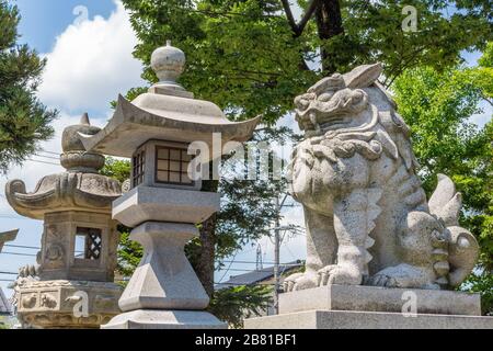 Cane-leone, o komainu, con lanterne di pietra, al santuario di Miumajinja shinto, Kanazawa, Giappone. Queste statue tradizionali sono viste a coppie nella maggior parte dei santuari A. Foto Stock