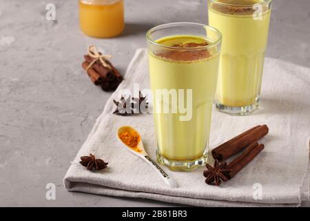 Latte curcuma dorato ayurvedico in vetro con polvere di curcuma, cannella e stella di anice su sfondo grigio, spazio copia Foto Stock