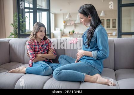 Ragazza in una camicia a scacchi che parla con la mamma incinta Foto Stock