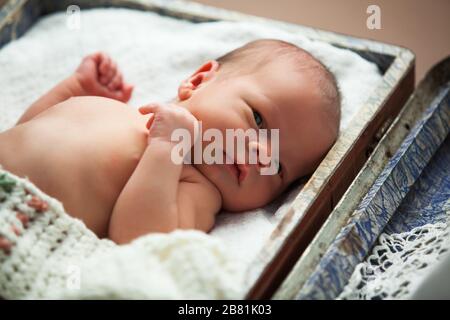 Primo piano del bambino neonato carino poggiato su fogli bianchi. Bambino dolce di pochi mesi che tiene le mani in pugni e guardando la macchina fotografica. Concetto di bambino carino Foto Stock