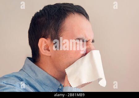 Il giovane uomo starnutisce in tessuto. Il ragazzo è malato, ha una reazione fredda o allergica. Coronavirus, epidemia 2020, malattia concetto. Businessman soffia il naso io Foto Stock