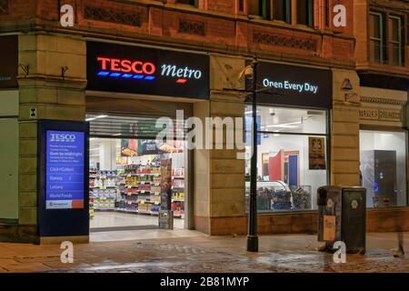 Manchester, Regno Unito, British Tesco Metro supermercato all'entrata del negozio. Vista notturna esterna dei negozi alimentari e del centro commerciale della città Foto Stock