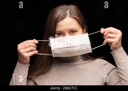 una donna indossa una maschera medica bianca dal coronavirus. protezione dalle infezioni, la dimostrazione. La medicina richiede l'uso di dispositivi di protezione Foto Stock