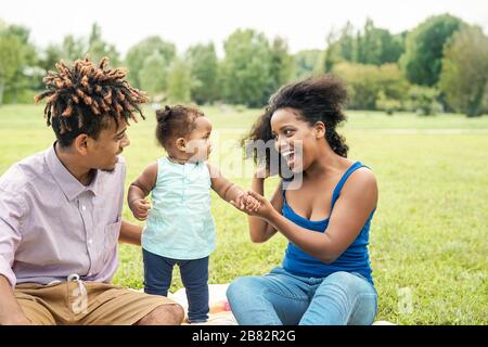 Felice famiglia africana divertirsi nel parco pubblico - madre e padre con la loro figlia godere insieme durante il fine settimana all'aperto Foto Stock