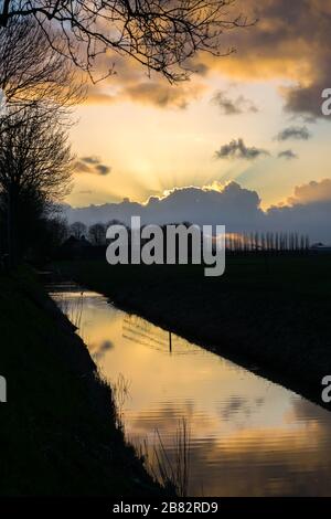 Sole raggi da dietro una nuvola durante il tramonto. Bei colori e riflessi nell'acqua. Foto Stock