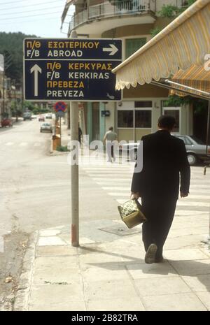 L'uomo greco porta i suoi acquisti sotto un cartello "all'estero" a Igoumenitsa, THESPROTIA, EPIRO, Grecia. Igoumenitsa è il principale porto di traghetti che serve la Grecia continentale nord-occidentale. I traghetti partono per le Isole IONIE e per l'Italia (o all'estero). Foto Stock