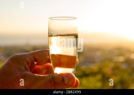 Bere un bicchiere di champagne di fronte a un meraviglioso paesaggio al tramonto, celebrando con felicità Foto Stock