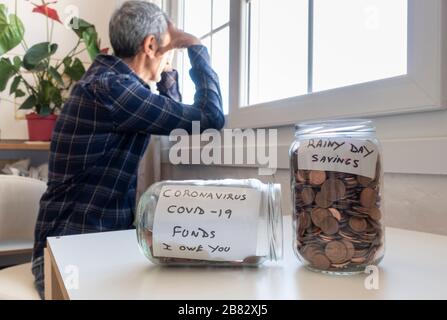 Uomo maturo che guarda fuori dalla finestra. Vasi di monete in primo piano. Fondi per coronavirus, risparmio, debito, preoccupazione, perdita di posti di lavoro... concetto Foto Stock