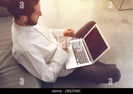 Giovane uomo d'affari seduto sul pavimento mentre lavori da casa con un computer portatile Foto Stock