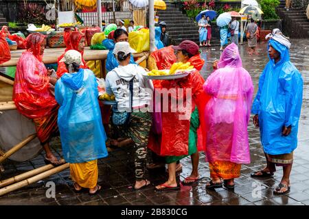 Donne locali che vendono mais/mais ai visitatori che indossano Ponchos durante UNA doccia a pioggia, la cerimonia di Batara Turun Kabeh, il tempio di Besakih, Bali, Indonesia. Foto Stock