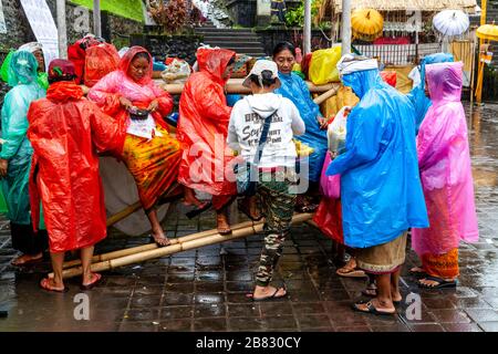 Donne locali che vendono mais/mais ai visitatori che indossano Ponchos durante UNA doccia a pioggia, la cerimonia di Batara Turun Kabeh, il tempio di Besakih, Bali, Indonesia. Foto Stock