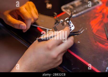 Un uomo sta riparando un telefono cellulare. Nel telaio, le sue mani e dettagli del dispositivo. Riparazione negozio di gadget Foto Stock