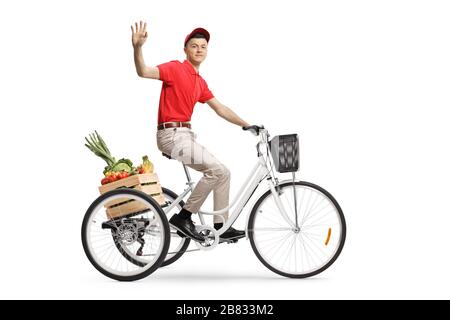 Giovane uomo che consegna i generi alimentari con un triciclo e che sventola alla camera isolata su sfondo bianco Foto Stock