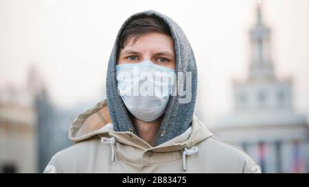 Ritratto ravvicinato giovane europeo uomo in maschera facciale monouso protettiva camminare all'aperto. Nuovo coronavirus (COVID-19). Concetto di assistenza sanitaria Foto Stock