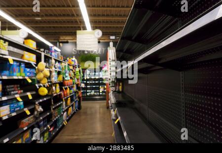 Scaffali di supermercato parzialmente vuoti a causa di panico che acquista e di sequestro di mancanza di carta igienica, asciugamano di carta, tovaglioli e prodotti per la pulizia, come risultato di pandemic scoppio di nuovo coronavirus a Toronto, Ontario, Canada il 19 marzo 2020. Punto focale stretto sul bordo del ripiano destro per sfocare i dettagli dei prodotti Foto Stock