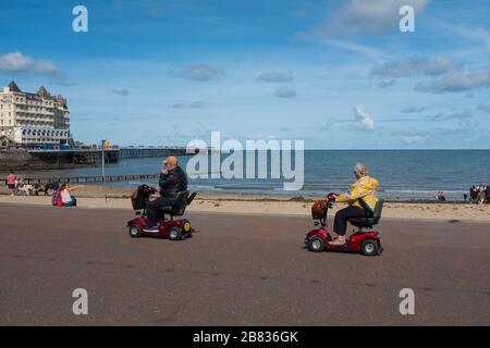 Uomo e donna su scooter per la mobilità sul lungomare di Llandudno, Galles, Regno Unito Foto Stock