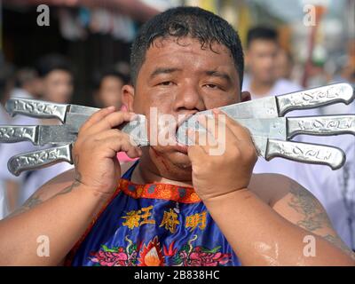 Il devoto taoista cinese thailandese in sovrappeso trafigge la guancia destra con sei coltelli in alluminio durante il Festival vegetariano di Phuket. Foto Stock