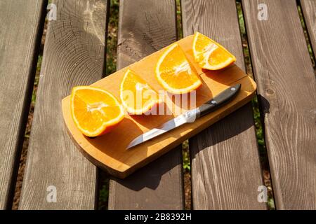 appetitosi pezzi tagliati di frutta d'arancia su tagliere su tavola marrone di legno sulle luci del sole con coltello. mangiare sano, frutta, estate tonica Foto Stock