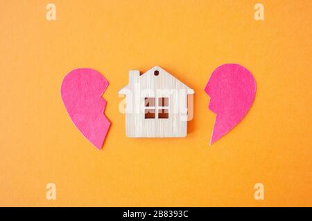 Divorzio, divisione della proprietà, povertà e nessun concetto di denaro. Casa di legno con cuore rotto su sfondo arancione brillante. Ipoteca, affitto, realtor Foto Stock
